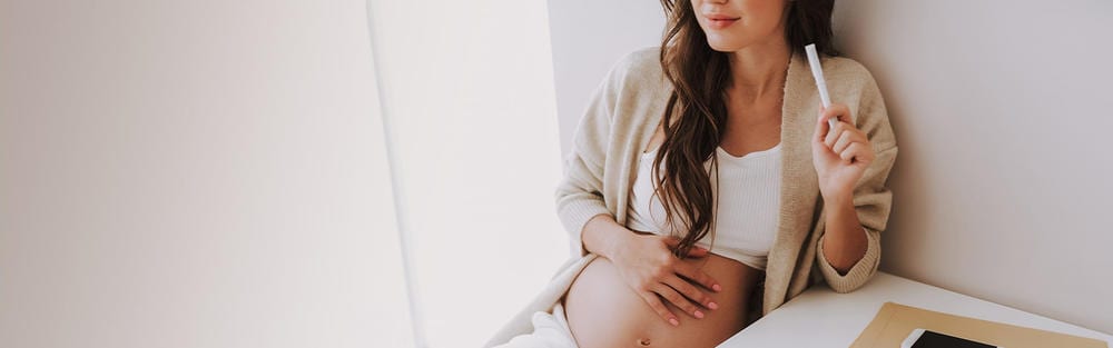 Atraktivna mlada trudnica drži ruku na trbuhu u svjetlom prostoru
